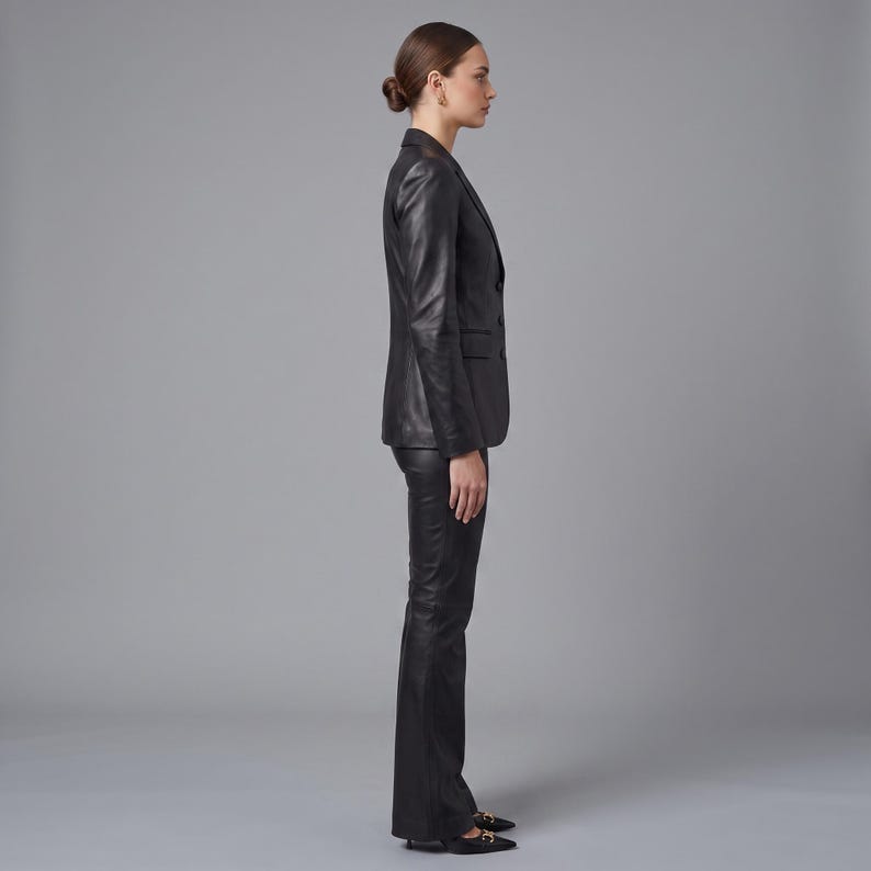 K&ouml;nnte beinhalten: Ein schwarzer Lederblazer mit steigendem Revers und drei Kn&ouml;pfen auf der Vorderseite, kombiniert mit einer passenden schwarzen Lederhose. Das Set hat eine glatte, polierte Oberfl&auml;che, lange &Auml;rmel und eine taillierte Passform, Seitenansicht.