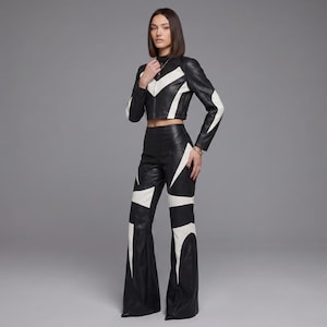 May include: A black and white leather two-piece set consisting of a cropped long-sleeve jacket with a high collar and a front zipper, paired with high-waisted flared trousers. Both pieces feature a bold, geometric white chevron and panel pattern.