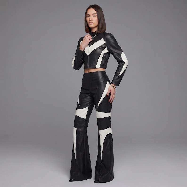 May include: A black and white leather two-piece set consisting of a cropped long-sleeve jacket with a high collar and a front zipper, paired with high-waisted flared trousers. Both pieces feature a bold, geometric white chevron and panel pattern.