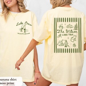 May include: A light yellow t-shirt with the text "Lake Crew" and "Vallecito Lake 2026" printed on the front. The back of the shirt features a green graphic with the text "The Wilson Lake Trip" and camping-themed illustrations.