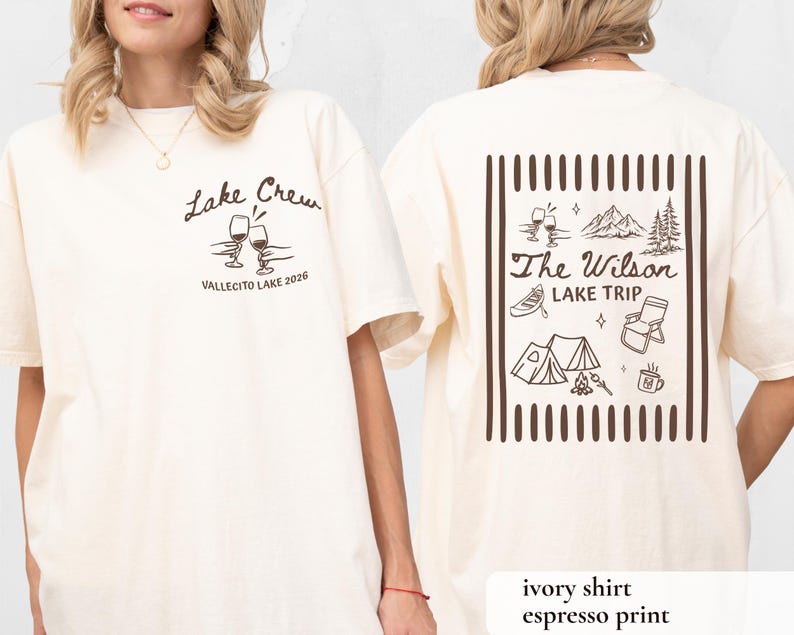 May include: Ivory-colored t-shirt with espresso-colored print. The front features "Lake Crew" text and wine glasses. The back displays "The Wilson Lake Trip" with camping and lake-themed illustrations. The shirt is a casual, unisex style.