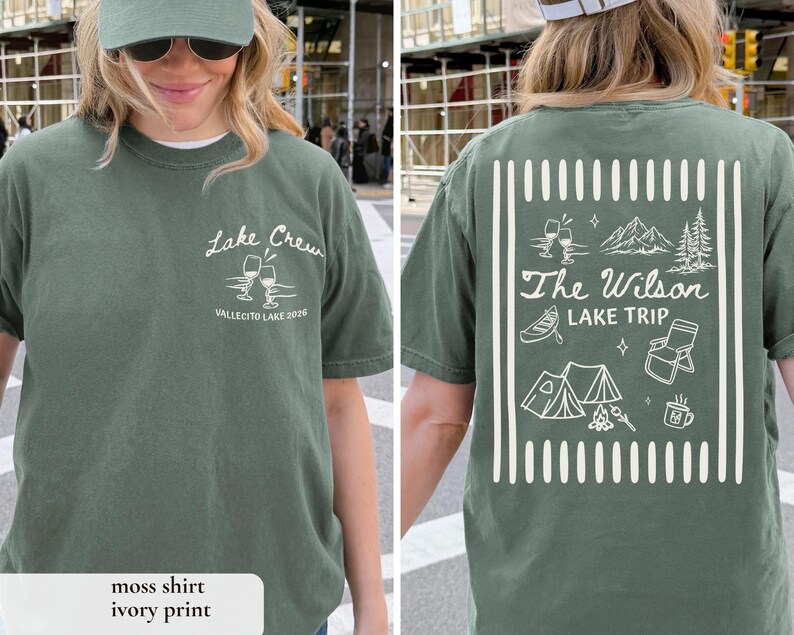 May include: A moss green t-shirt with white text and graphics. The front of the shirt says "Lake Crew" with wine glasses and "Vallecito Lake 2026". The back says "The Wilson Lake Trip" with camping-themed illustrations.