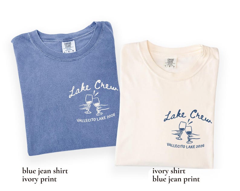 May include: Two folded t-shirts, one blue and one ivory, each with the text "Lake Crew" and "VALLECITO LAKE 2026" printed on them. The design includes two wine glasses. The blue shirt has an ivory print, and the ivory shirt has a blue print.