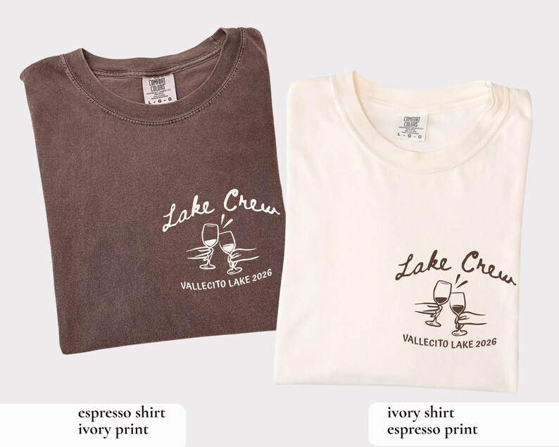May include: Two folded t-shirts, one espresso-colored and one ivory, each with a crew neck. Both shirts feature the text "Lake Crew" and a graphic of two wine glasses, with "VALLECITO LAKE 2026" below.