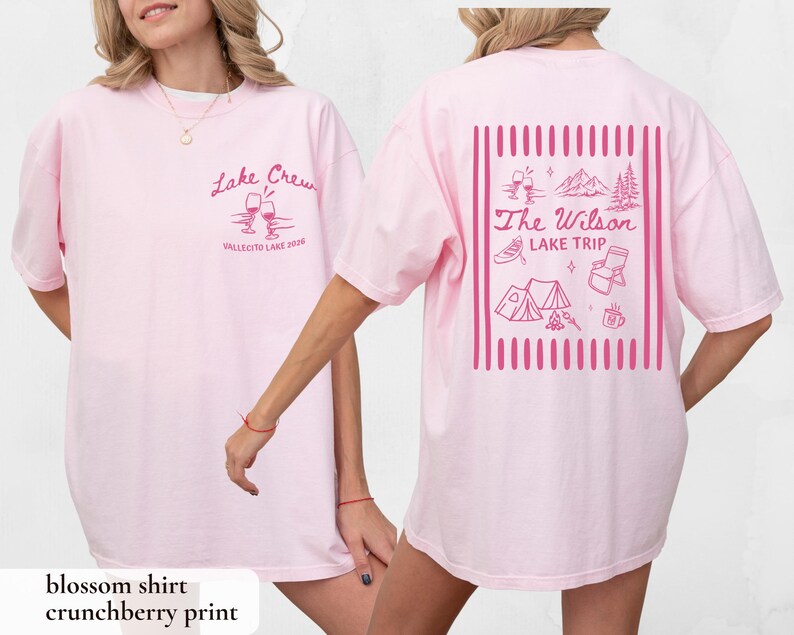 May include: Light pink t-shirt with the text "Lake Crew" and "Vallecito Lake 2020" in pink script on the front. The back of the shirt features a pink graphic with the text "The Wilson Lake Trip" and camping-themed illustrations.