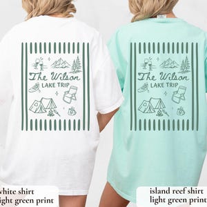 May include: White and island reef t-shirts with a light green graphic on the back. The graphic includes the text "The Wilson Lake Trip" with illustrations of mountains, a tent, a canoe, and other camping-themed elements.