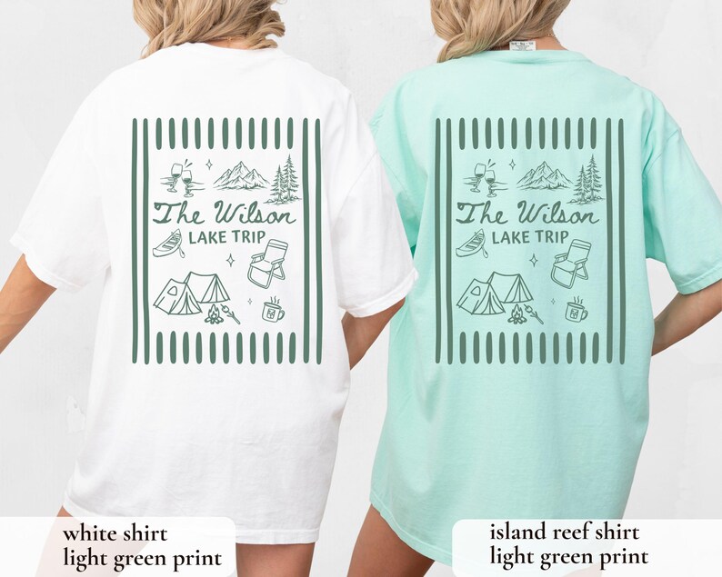 May include: White and island reef t-shirts with a light green graphic on the back. The graphic includes the text "The Wilson Lake Trip" with illustrations of mountains, a tent, a canoe, and other camping-themed elements.