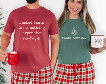 May include: A red t-shirt with the white text I asked Santa for something expensive and a green t-shirt with a white line-art Christmas tree and the text Santa sent me. Both shirts are paired with red and green plaid pyjama trousers.