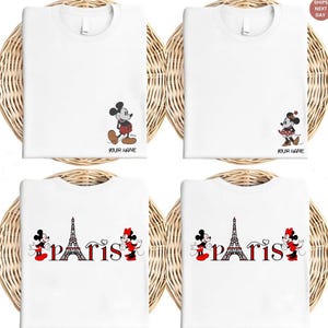 May include: White t-shirts featuring Mickey Mouse and Minnie Mouse designs. Some shirts have the Eiffel Tower with the word "Paris". Each shirt has the option to add a name. The shirts are displayed on a woven background.