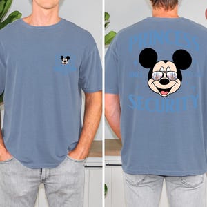 May include: A blue short-sleeved t-shirt featuring a Mickey Mouse graphic on the front and back. The front has a small Mickey Mouse design, while the back displays a larger Mickey Mouse wearing sunglasses with the text "PRINCESS SECURITY".