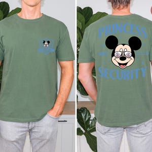 May include: Green t-shirt with a Mickey Mouse graphic on the front pocket and back. The back of the shirt features Mickey Mouse wearing sunglasses with the words "PRINCESS SECURITY".