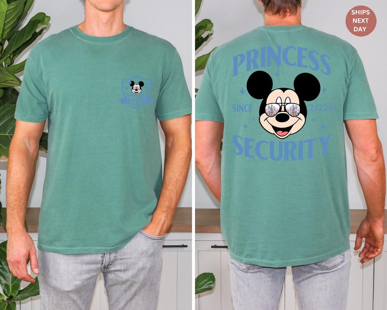 May include: A teal green t-shirt featuring a Mickey Mouse graphic. The front pocket has a small Mickey Mouse design. The back of the shirt displays "PRINCESS SECURITY" with Mickey wearing sunglasses. The shirt is a comfortable, casual style.
