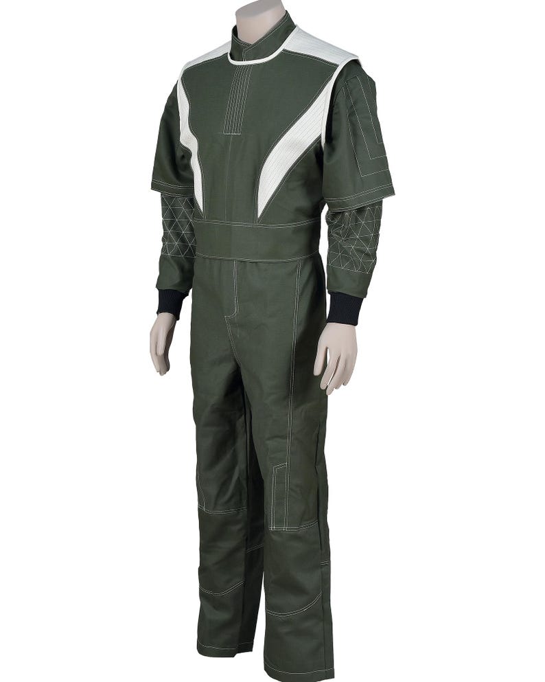 May include: A dark olive green jumpsuit featuring white paneling on the shoulders and chest, a high collar, and white contrast stitching throughout. The sleeves have a geometric triangular pattern, and the cuffs are finished with black fabric.