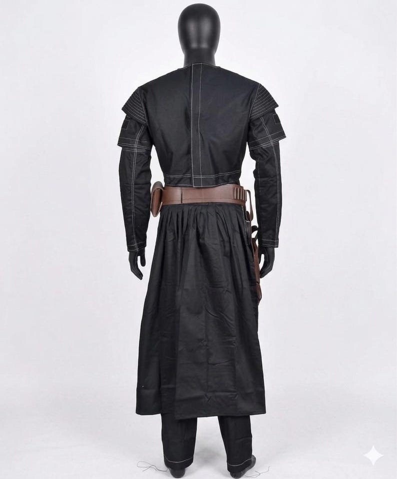 K&ouml;nnte beinhalten: Schwarzes Kost&uuml;m mit langem Mantel, lang&auml;rmliger Jacke und Hose. Die Jacke hat wei&szlig;e N&auml;hte und Schulterakzente. Ein brauner G&uuml;rtel und ein Holster werden um die Taille getragen. Das Outfit wird auf einer schwarzen Schaufensterpuppe pr&auml;sentiert.