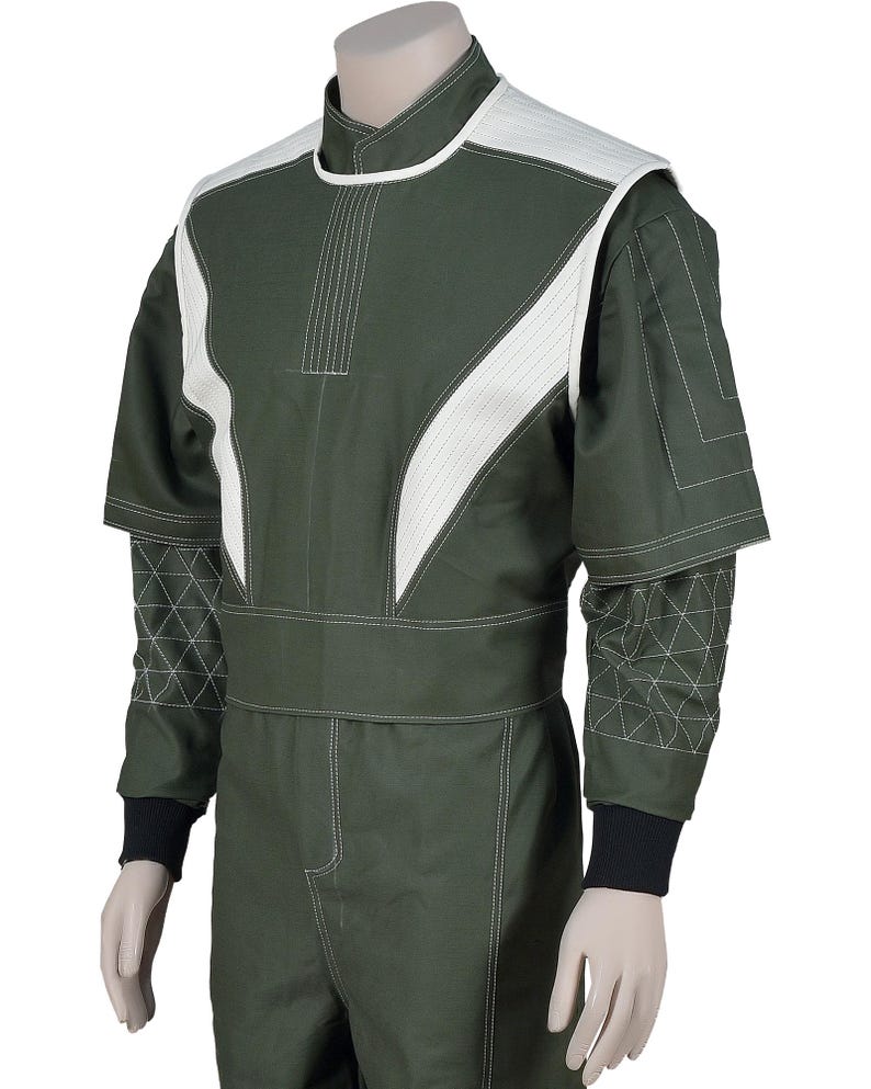 May include: An olive green jumpsuit featuring a high collar, white textured shoulder panels, and white contrast stitching. The sleeves have a geometric quilted pattern on the forearms, short layered sleeves, and black ribbed cuffs at the wrists.