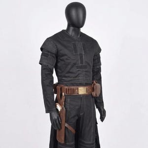K&ouml;nnte beinhalten: Schwarzes Kost&uuml;m mit braunem G&uuml;rtel und Holster. Das Kost&uuml;m hat ein lang&auml;rmliges Oberteil mit vertikalen N&auml;hten und eine passende Hose. Der G&uuml;rtel hat eine goldene Schnalle und ein braunes Holster mit einem wei&szlig;en Gegenstand.
