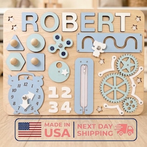 Könnte beinhalten: Holz-Lernspielbrett mit dem Namen "ROBERT" in blauen und weißen Buchstaben. Enthält interaktive Elemente wie Formen, Zahnräder, eine Uhr, einen Reißverschluss und Zahlen. Für frühes Lernen und sensorische Erkundung. Maße in Zentimetern.