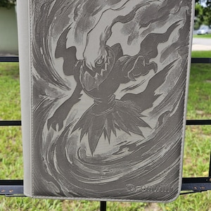 May include: A grey rectangular trading card binder featuring an embossed illustration of the Pokémon Darkrai surrounded by swirling wind effects. The cover has a textured surface and includes the brand name Vault X printed in the bottom corner.