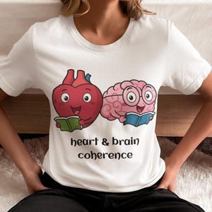 May include: White t-shirt featuring a cartoon heart and brain, both reading books. The heart is red, and the brain is pink with glasses. The text "heart & brain coherence" is printed below the illustrations.