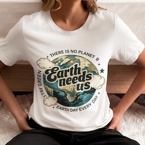 Könnte beinhalten: Weißes T-Shirt mit Rundhalsausschnitt und einem Erd-Grafik-Aufdruck mit dem Text "Earth needs us". Das Shirt enthält auch die Sätze "There is no planet B", "Stay Green" und "Earth Day Every Day".