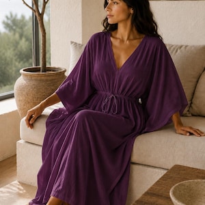 Puede incluir: Un vestido caft&aacute;n de color morado intenso con escote en V, mangas anchas estilo kimono y cintura el&aacute;stica con cord&oacute;n ajustable. La prenda es larga hasta el suelo, con una falda suelta y fluida y un acabado de tela suave y texturizada.