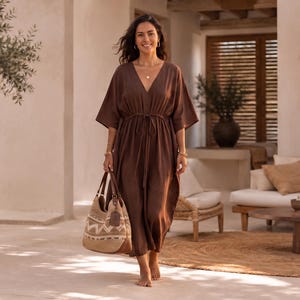 May include: A dark brown kaftan dress with a V-neckline, wide sleeves, and a drawstring waist, paired with a beige and brown woven tote bag featuring a geometric pattern and a brown leather tag, worn with gold hoop earrings and layered necklaces.