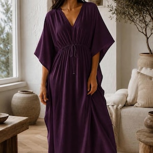 Puede incluir: Un vestido caft&aacute;n largo de color morado intenso con escote en V, mangas anchas estilo kimono y cintura con cord&oacute;n ajustable y lazos finos. La prenda est&aacute; confeccionada en tela de color s&oacute;lido con textura sutil y silueta fluida.