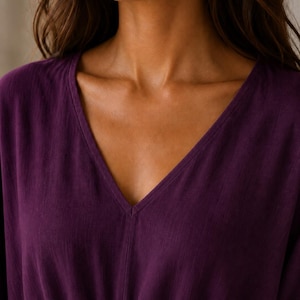 Puede incluir: Una blusa de color morado intenso con escote en V y detalle de cord&oacute;n ajustable en la cintura. La prenda est&aacute; confeccionada en un tejido texturizado con patrones de tejido vertical visibles, presentando un dise&ntilde;o sencillo de manga larga.