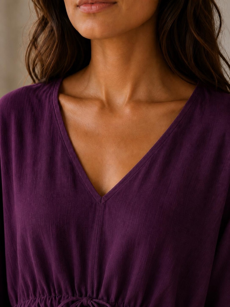 Puede incluir: Una blusa de color morado intenso con escote en V y detalle de cord&oacute;n ajustable en la cintura. La prenda est&aacute; confeccionada en un tejido texturizado con patrones de tejido vertical visibles, presentando un dise&ntilde;o sencillo de manga larga.