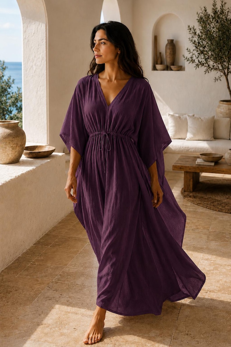 Puede incluir: Un vestido caft&aacute;n largo de color morado intenso con escote en V, mangas anchas estilo kimono y cintura con cord&oacute;n ajustable y lazos finos. La prenda est&aacute; confeccionada con un tejido ligero y texturizado que cae holgadamente hasta los tobillos.