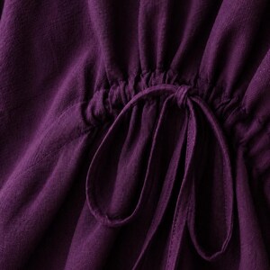 Puede incluir: Una prenda de color morado intenso con un detalle de cintura fruncida mediante cord&oacute;n. La tela tiene un tejido texturizado visible y el cord&oacute;n est&aacute; atado en un lazo en el centro, creando suaves pliegues verticales sobre la superficie.