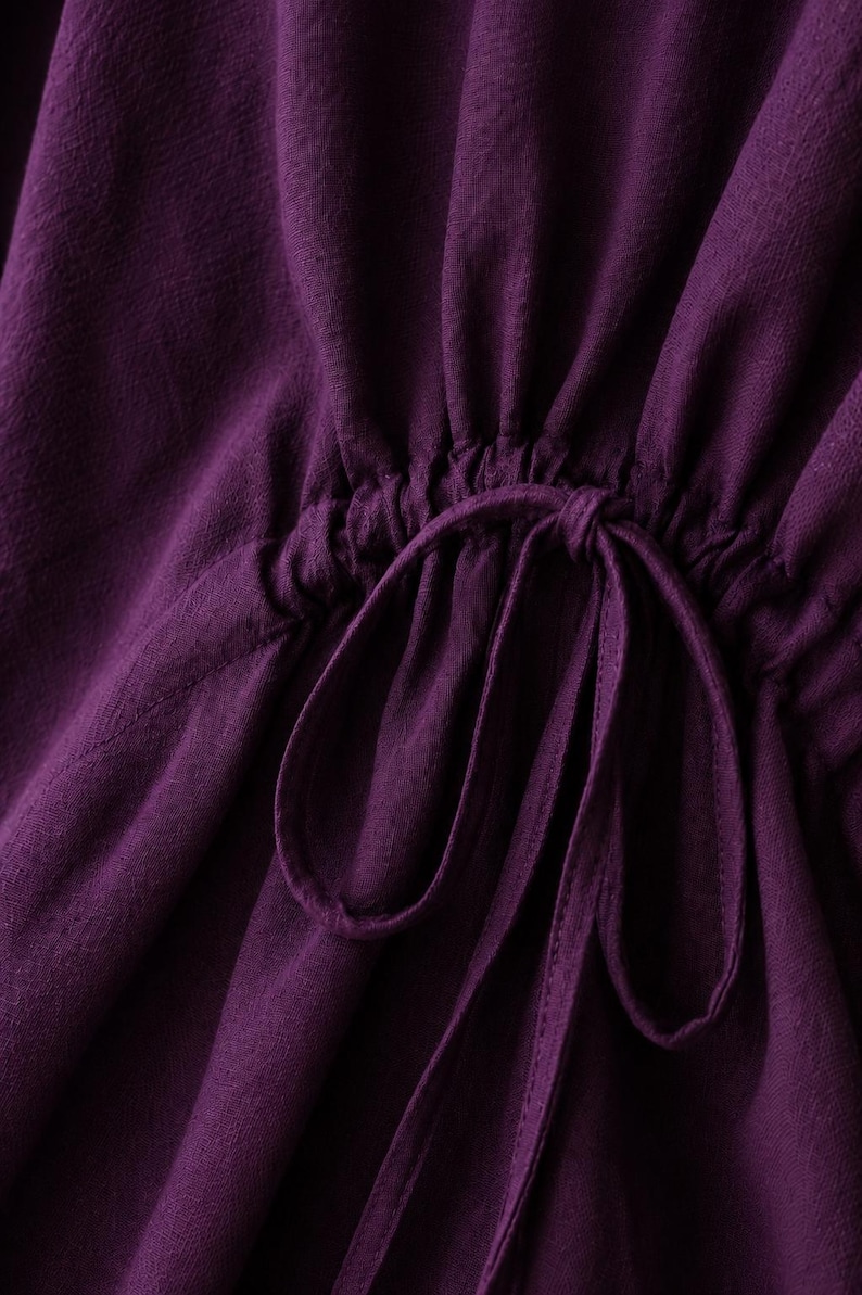 Puede incluir: Una prenda de color morado intenso con un detalle de cintura fruncida mediante cord&oacute;n. La tela tiene un tejido texturizado visible y el cord&oacute;n est&aacute; atado en un lazo en el centro, creando suaves pliegues verticales sobre la superficie.