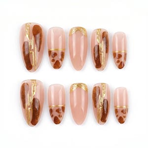 May include: A set of ten almond-shaped false nails. The nails feature a nude base with brown and gold accents. Some nails have a gold stripe across the top, while others have brown and gold patterns.