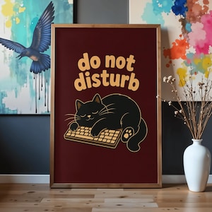 May include: A framed vertical poster with a dark maroon background featuring a black cat sleeping on a computer keyboard. Above the cat, the text reads "do not disturb" in a rounded, light yellow font. The cat has closed eyes and visible paw pads.