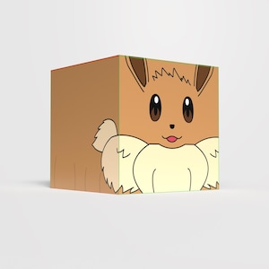Puede incluir: Un cubo marrón con el personaje Eevee de la franquicia Pokémon. El cubo tiene la cara de Eevee en un lado, con orejas marrones, ojos marrones grandes y una lengua rosa. El diseño del cubo es una ilustración de dibujos animados.