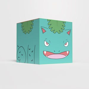 Puede incluir: Un cubo turquesa con una ilustración de dibujos animados del personaje Bulbasaur. El diseño incluye la cara del personaje, con ojos rojos, una boca muy abierta y hojas verdes en la parte superior. El cubo es de color sólido.
