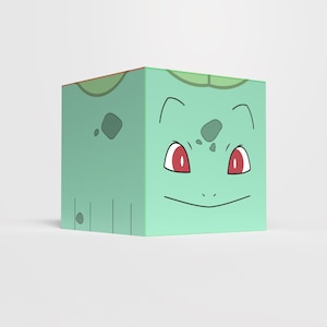 Puede incluir: Un cubo verde claro con una cara de dibujos animados, ojos rojos y una boca sonriente delineada en negro. El cubo tiene manchas de color verde oscuro y un diseño de hoja en la parte superior, que se asemeja a un personaje popular.