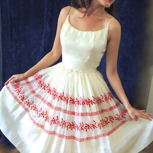 May include: A white sleeveless dress with red embroidered floral details and a full skirt.