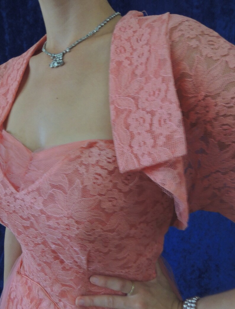 Puede incluir: Un vestido vintage de encaje color melocot&oacute;n con un bolero a juego. El vestido presenta un escote coraz&oacute;n y un corpi&ntilde;o ajustado. Un collar plateado brillante a&ntilde;ade un toque de elegancia. Perfecto para una ocasi&oacute;n especial.