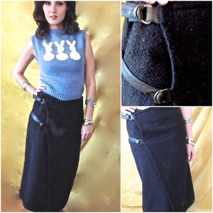 May include: A woman wearing a blue sweater with a white bunny rabbit design and a black wrap skirt with a leather belt. The skirt has two straps that wrap around the waist and buckle at the side.
