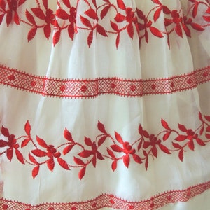 May include: White fabric with red embroidered floral designs. The fabric has a delicate, sheer texture and features a red lace trim.
