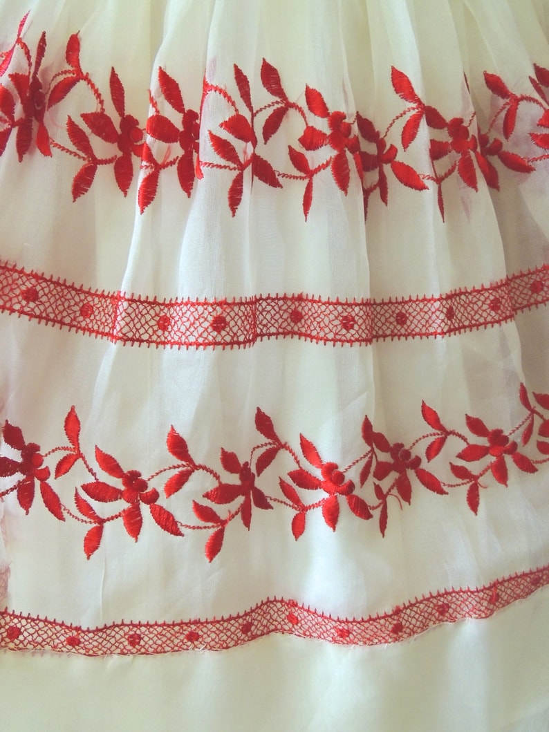May include: White fabric with red embroidered floral designs. The fabric has a delicate, sheer texture and features a red lace trim.