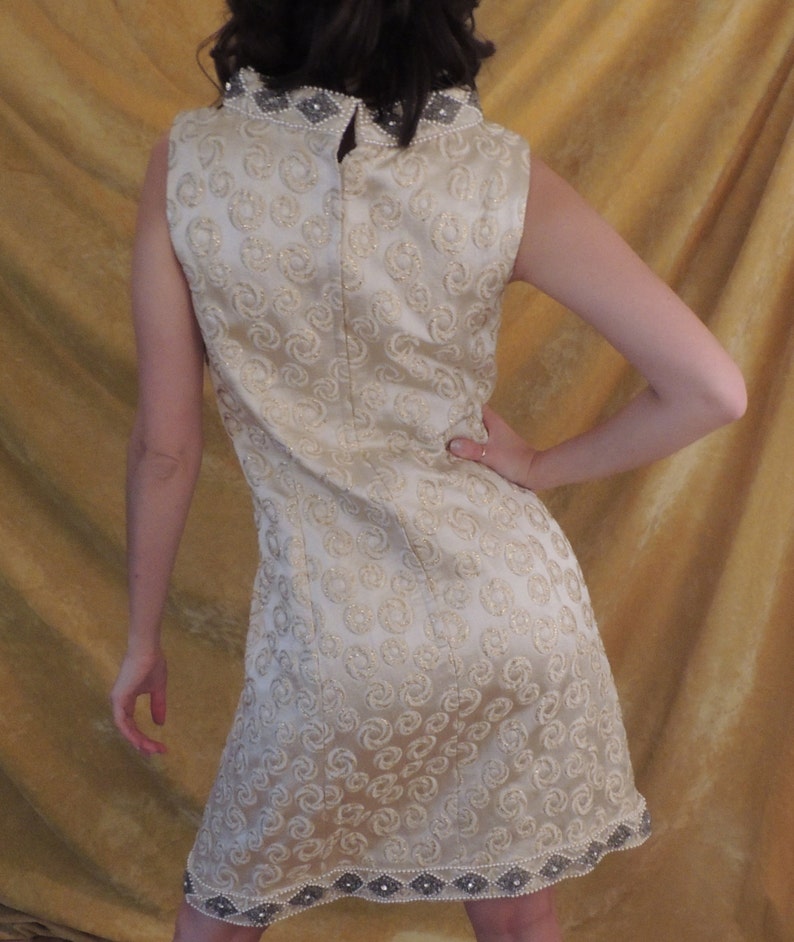 Puede incluir: Un vestido sin mangas con cuello alto y un ribete de cuentas. El vestido est&aacute; hecho de una tela blanca con un sutil patr&oacute;n de espiral.