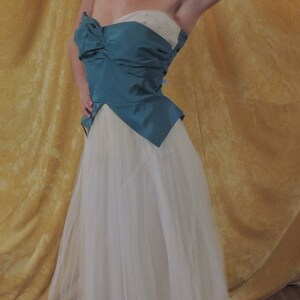 Puede incluir: Vestido de fiesta sin tirantes en verde azulado y marfil. El corpi&ntilde;o es verde azulado con un detalle de lazo, y la falda es de tul marfil fluido. El vestido es de estilo vintage, adecuado para una ocasi&oacute;n especial.