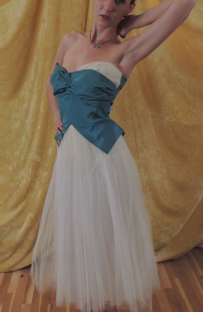 Puede incluir: Vestido de fiesta sin tirantes en verde azulado y marfil. El corpi&ntilde;o es verde azulado con un detalle de lazo, y la falda es de tul marfil fluido. El vestido es de estilo vintage, adecuado para una ocasi&oacute;n especial.