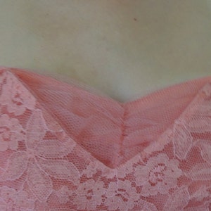 Puede incluir: Un vestido sin tirantes de color coral con escote coraz&oacute;n. El vestido presenta una delicada superposici&oacute;n de encaje floral, que a&ntilde;ade textura y detalles. El corpi&ntilde;o es entallado y el vestido parece estar hecho de una tela suave y fluida.