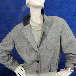 May include: A cropped gray and white houndstooth blazer with a black collar and a black button closure. The blazer has a cinched waist and long sleeves with black button cuffs.