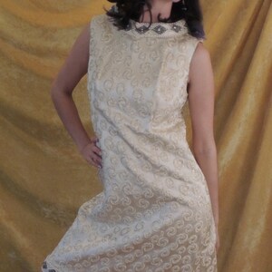 Puede incluir: Un vestido blanco sin mangas con un escote de cuentas y un patr&oacute;n de remolino. El vestido tiene un ribete de cuentas alrededor del dobladillo.