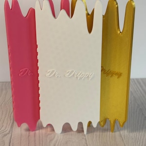 May include: Three colorful, vertical, decorative panels. The panels are pink, white, and gold. The text "Dr. Drippy" is embossed on the white panel. The panels have a wavy top edge and a textured surface.