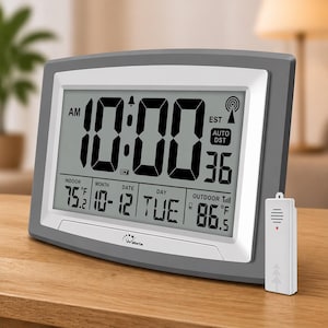 May include: A grey digital clock showing 10:00 AM, with indoor and outdoor temperatures in Fahrenheit. The clock displays the date, day, and a wireless signal icon. A small white remote sensor is positioned beside the clock.